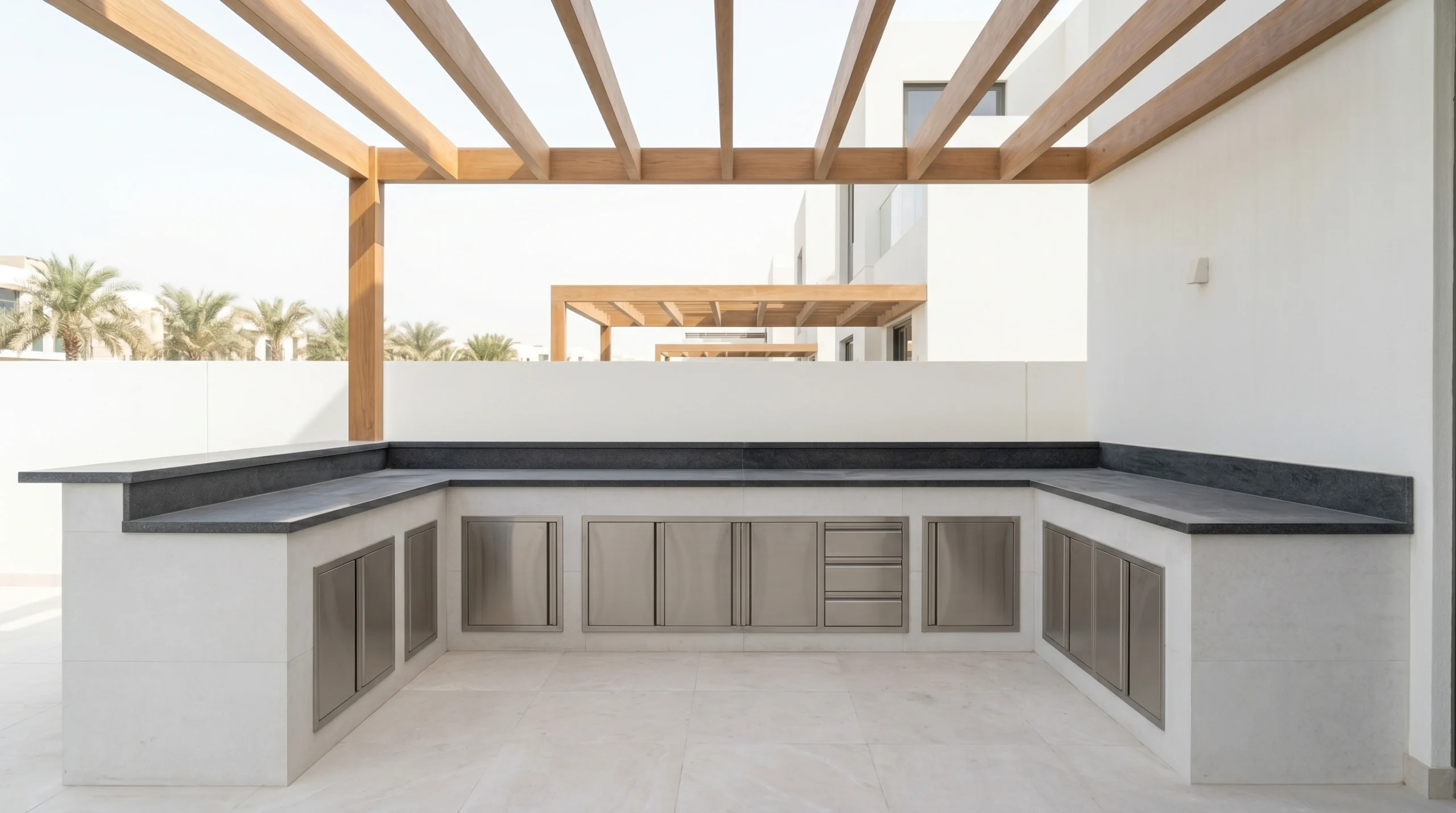 Custom L-shaped outdoor kitchen in porcelain tile cladding with granite countertop and stainless cabinet doors on a Dubai villa terrace by Karnak Carpentry