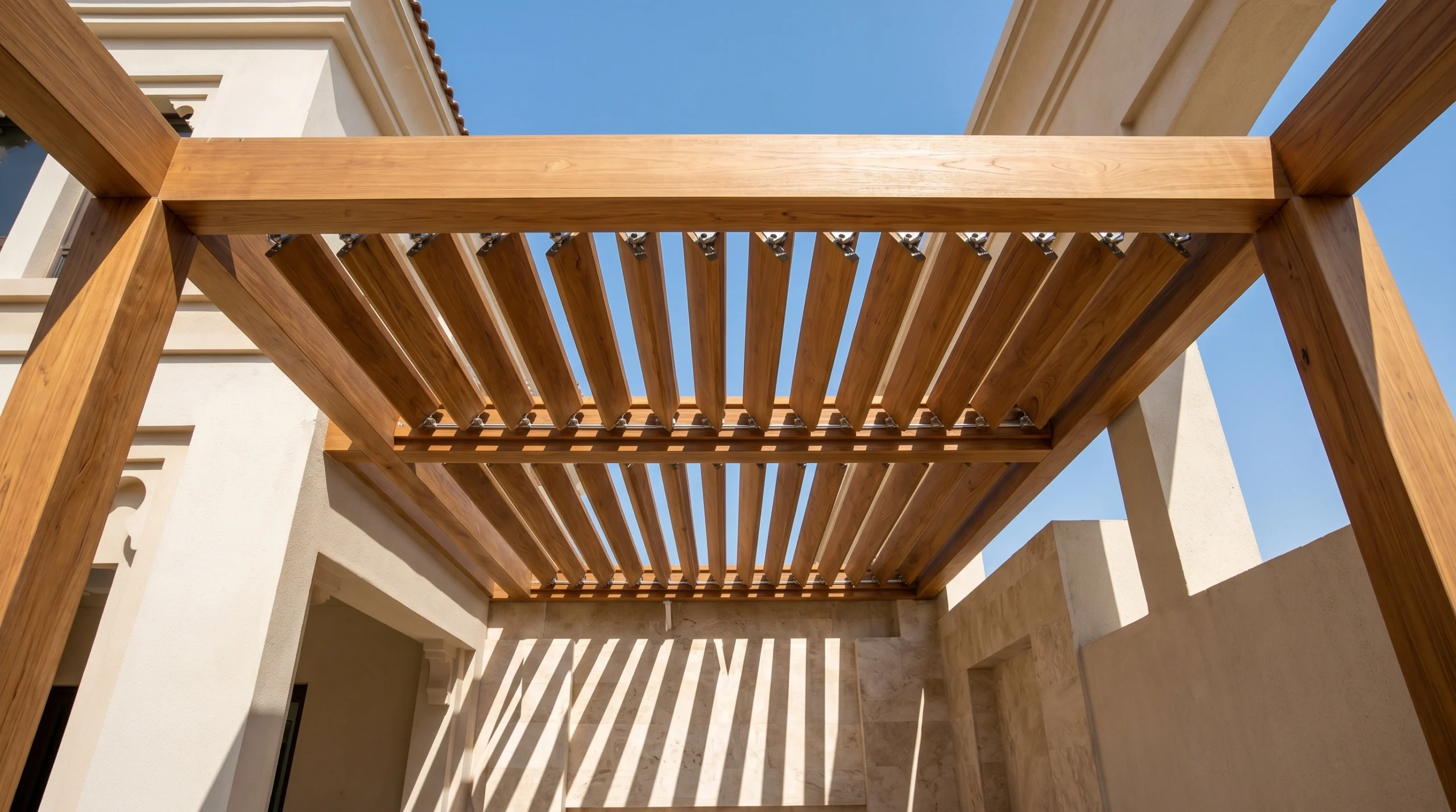 Custom adjustable teak louvred pergola roof casting striped shadows over a Dubai villa patio by Karnak Carpentry