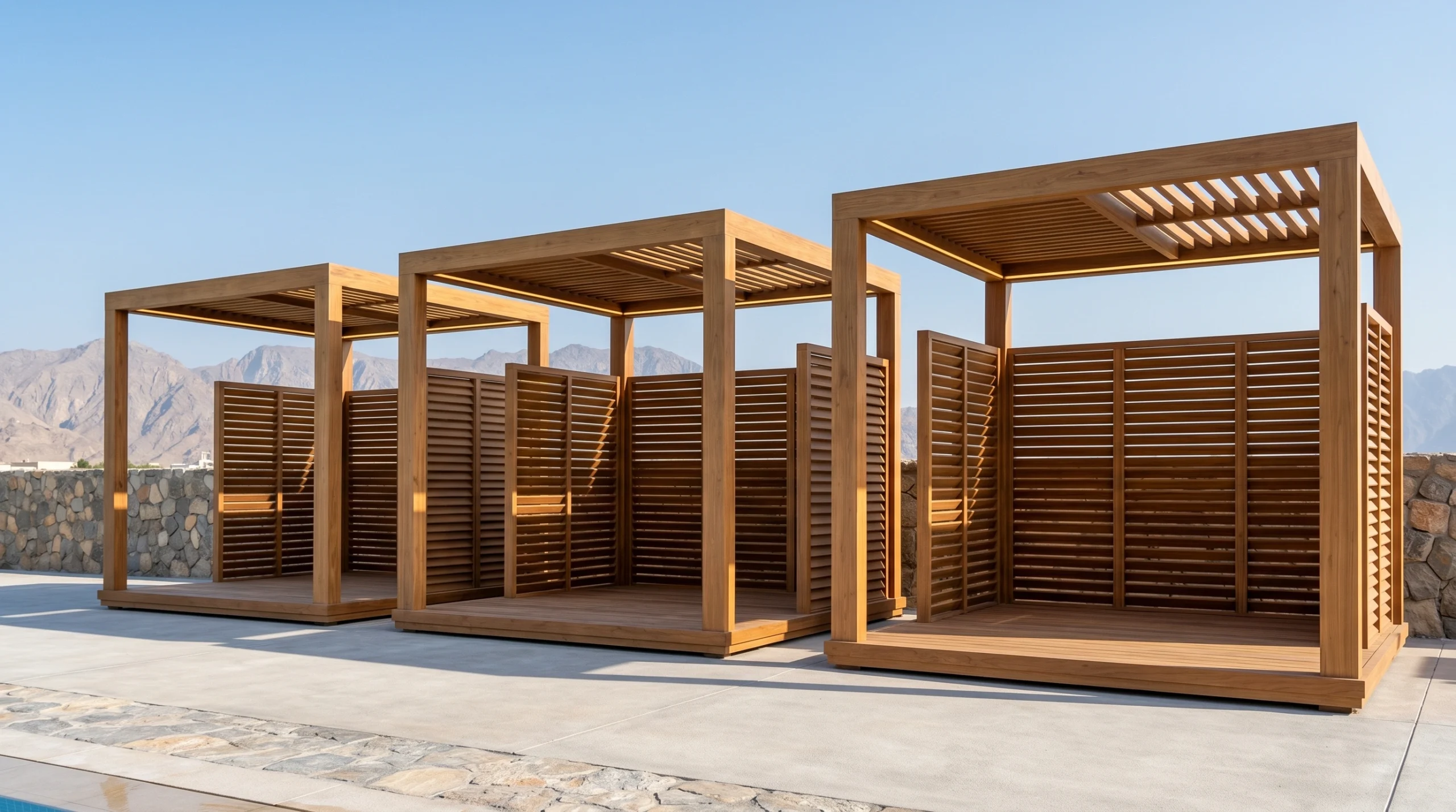Cluster of three custom teak poolside cabanas with louvred roofs, slatted privacy screens, and integrated LED lighting at a RAK resort by Karnak Carpentry