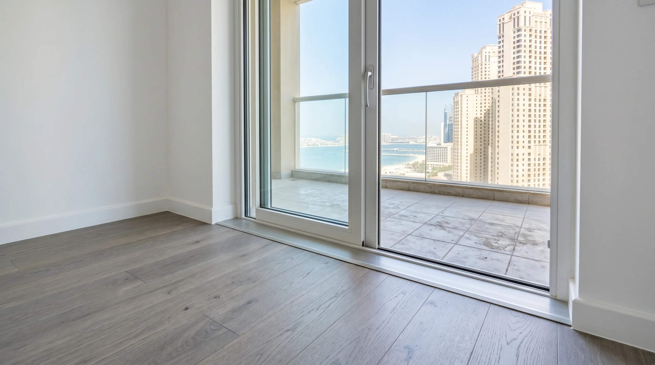 Moisture-resistant grey-washed oak hardwood flooring installed at JBR Dubai apartment balcony threshold with precision aluminium transition strip remediation